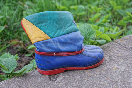 one old colored leather boot stands on gray asphalt on the street near green vegetation
