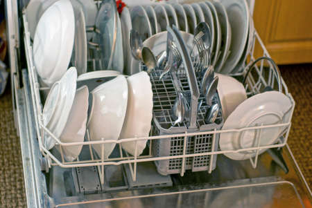 a set of kitchen utensils made of white plates and metal spoons and forks in a dishwasher drawer in the kitchenの写真素材