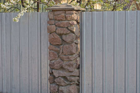 part of a fence wall made of brown stone and gray metal on a city streetの写真素材