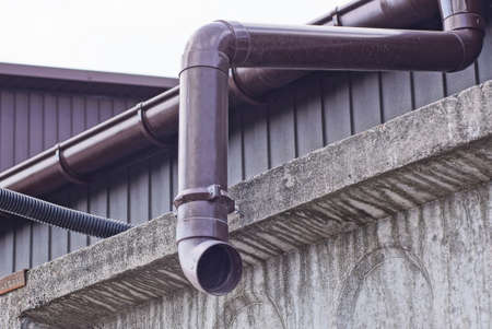 brown plastic drainpipe on the wall above the gray concrete fence outsideの写真素材