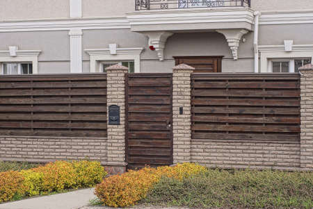 closed brown wooden door on the wall of a fence made of bricks and boards on the street in green...