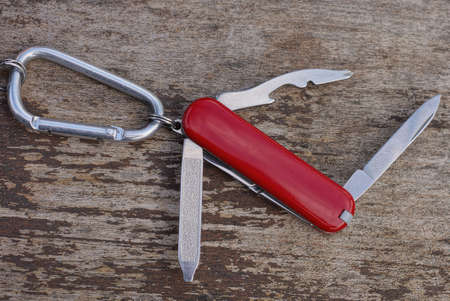 one small red open multitool knife with open gray blades on an iron latch carabiner lies on a brown...