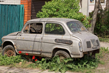 one old gray passenger car stands in green grass and red flowers on the street against the wall