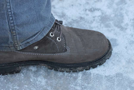 one brown leather shoe on a leg in gray jeans on a winter street on white snow