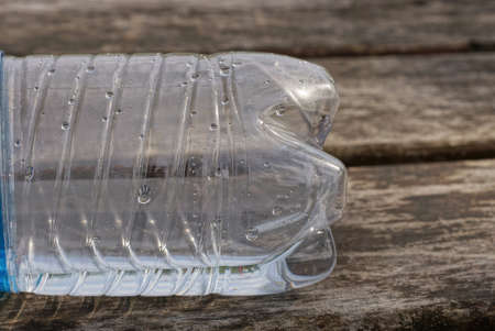a piece of a white empty one wet plastic bottle lies on a gray wooden table