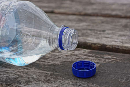 one white open plastic bottle with water and a blue stopper lies on a gray wooden tableの写真素材