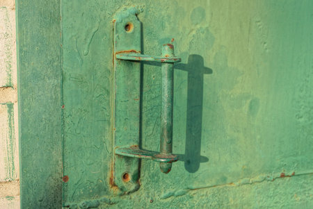 one green metal doorknob on a iron dirty door and a wall on the streetの写真素材