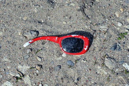 one piece of old broken red brown sunglasses lies on the gray sand in the streetの写真素材
