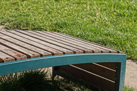 one empty brown wooden bench stands in green grass by a gray sidewalk in a park