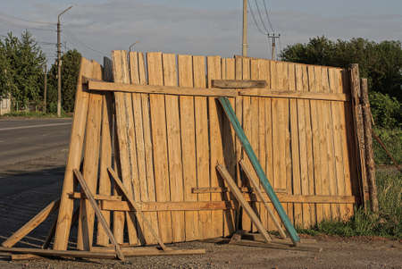 part of a brown old broken wooden fence on the street near a gray asphalt road