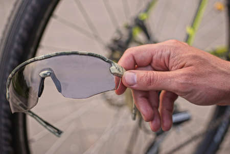 hand holds a gray sunglasses on the street against the background of the wheel of a sports bike