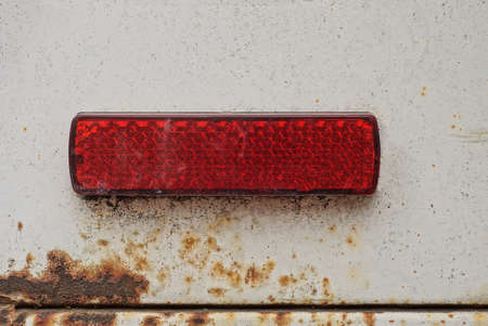 one old small rectangular red plastic turn signal reflector on white car metal in brown rustの写真素材