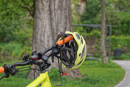 part of a sports bike with a black steering wheel and a yellow helmet on the street in a summer park