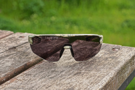 one gray sunglasses lies on a brown wooden table outdoors on a green backgroundの写真素材