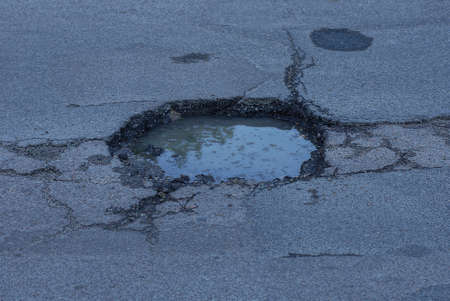 one pit pothole with dirty water on the gray asphalt road on the streetの写真素材