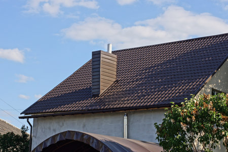 one big metal chimney on a brown tiled roof of a private house against a blue sky