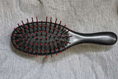 one big plastic black dirty hairbrush lies on a gray crumpled cloth