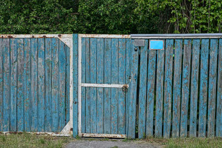 Blue old wooden fence and closed doors on the rural street near the roadの写真素材