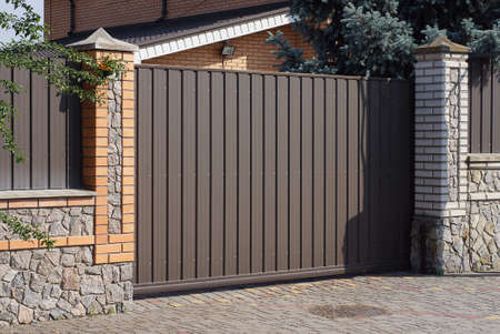 one large closed metal brown gate on a brick stone fence wall outdoors on a gray pavementの写真素材
