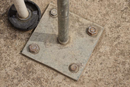 gray square iron plate with pipe bolted into concrete floor outdoors