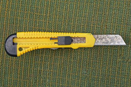 one yellow black stationery knife with a blade lies on a green table