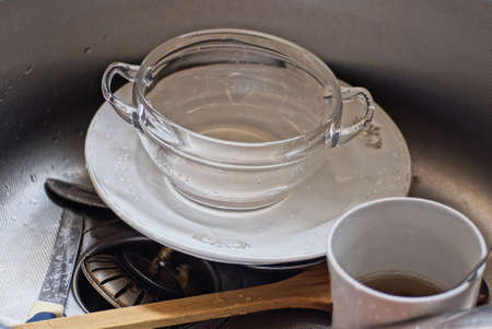 a pile of dirty dishes from a cup and white plates in a gray metal sink in the kitchen