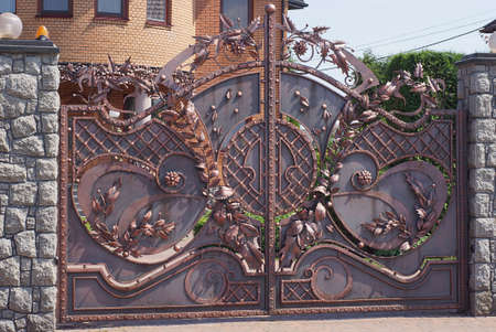 one large brown metal gate with a forged pattern on a gray stone wall of a fence in the street
