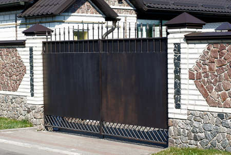 one black metal gate on a fence wall made of white bricks and brown stones on a rural street