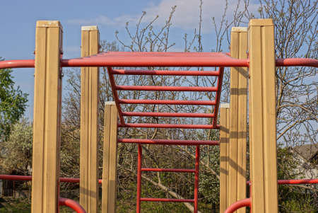 a sports ground with a red metal horizontal bar and an iron ladder on brown wooden poles on the...