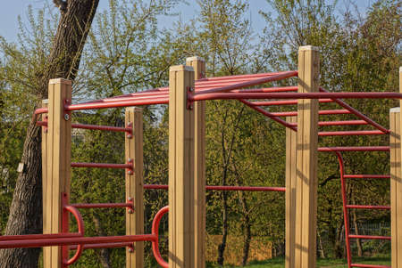 a sports ground with a red metal horizontal bar and an iron ladder on brown wooden poles on the...