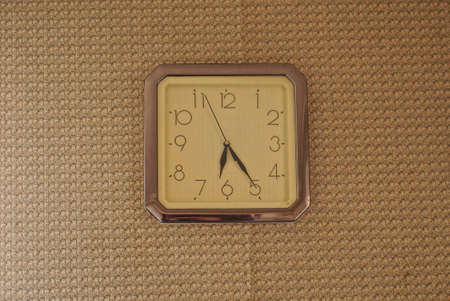 one gray square clock hanging on a brown wall in a room