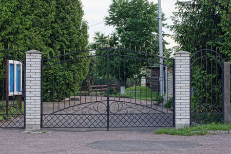 black metal gates made of black wrought iron rods and part of a fence made of white bricks in green...