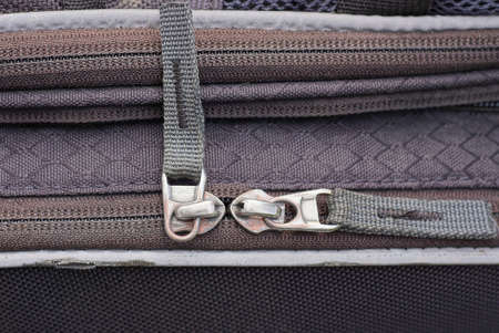 two white closed metal zips on the gray fabric of an old bag