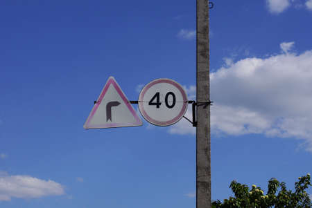 two road signs speed limit and no turning is hanging on a concrete pole on the street against the blue skyの写真素材