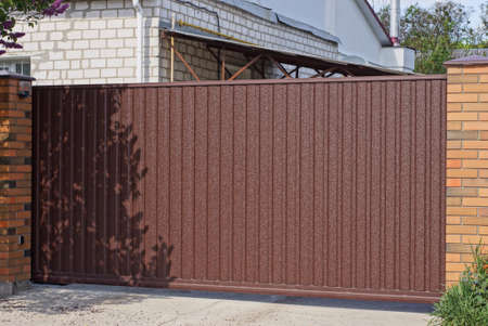 one big brown metal gate and part of the wall of the fence made of boards and bricks on the street