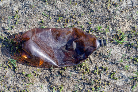 one old brown plastic bottle lies on gray ground and grass on natureの写真素材