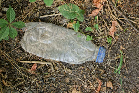 garbage from one big white plastic bottle lies on a gray ground in nature