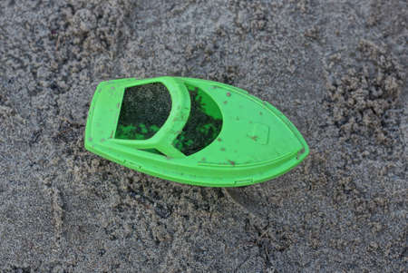 one dirty green plastic small boat toy stands on gray sand in a sandbox outsideの写真素材