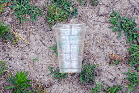 garbage from one big empty white plastic cup lies on the gray ground and in the green grass in...
