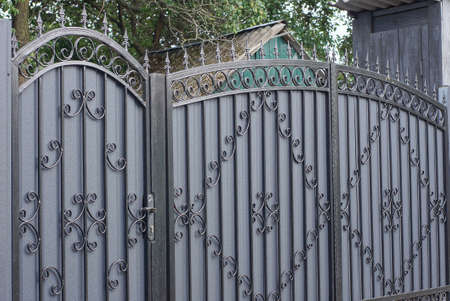 gray metal door and large closed gate with black wrought iron pattern with sharp bars on a rural...