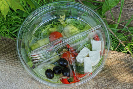 fresh greek salad food in a transparent bowl with sunflower oil and a plastic white fork stands on a...