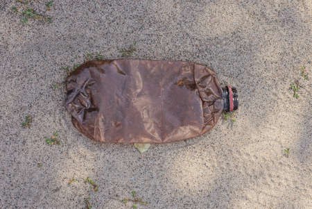 garbage from one dirty brown plastic bottle lies on the gray sand in the street