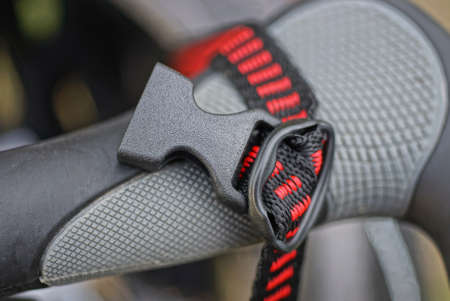 one open plastic latch on a black red harness on a gray bicycle handlebar