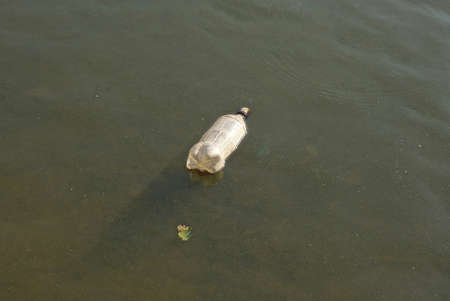 one old white plastic bottle lies in the gray water of the lake in natureの写真素材