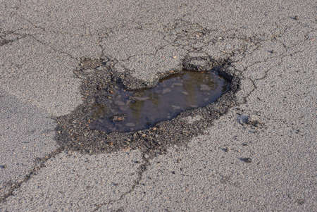 one small pit pothole with dirty water on the gray asphalt road on the street