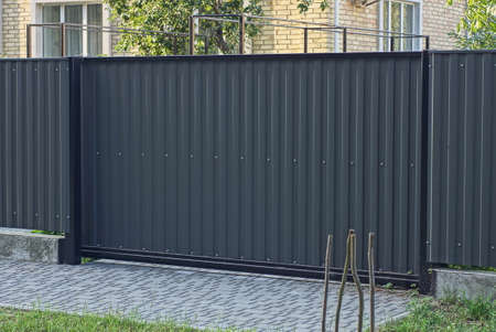 one big closed metal black gate and part of a iron fence wall on a rural street