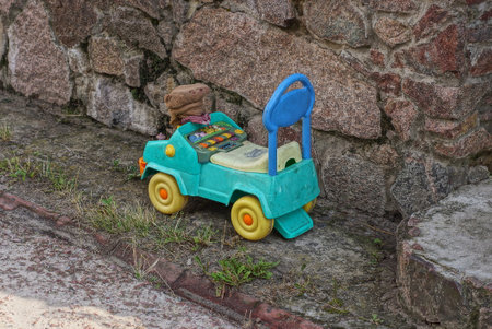 one toy plastic colored car bike stands on the grass near a gray stone wall on the streetの写真素材