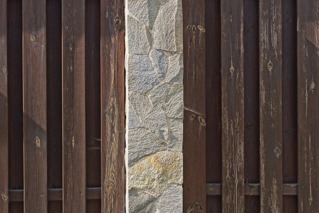 texture of brown wooden boards and gray stone pillar in the wall of the fence