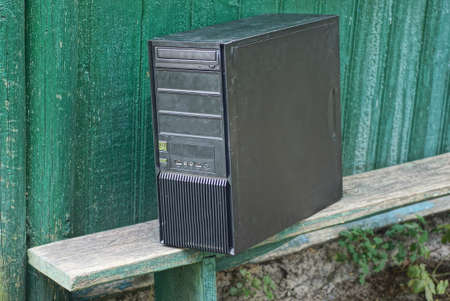 one old black metal computer stands on a gray wooden table against a green wall in the streetの写真素材