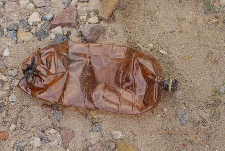 garbage from one big dirty brown plastic bottle lies on the gray sand in the streetの写真素材